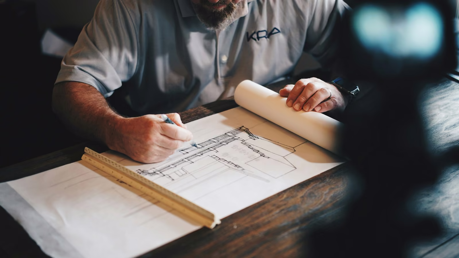 Arquitecto trazando un plano con regla y lápiz sobre su mesa de trabajo