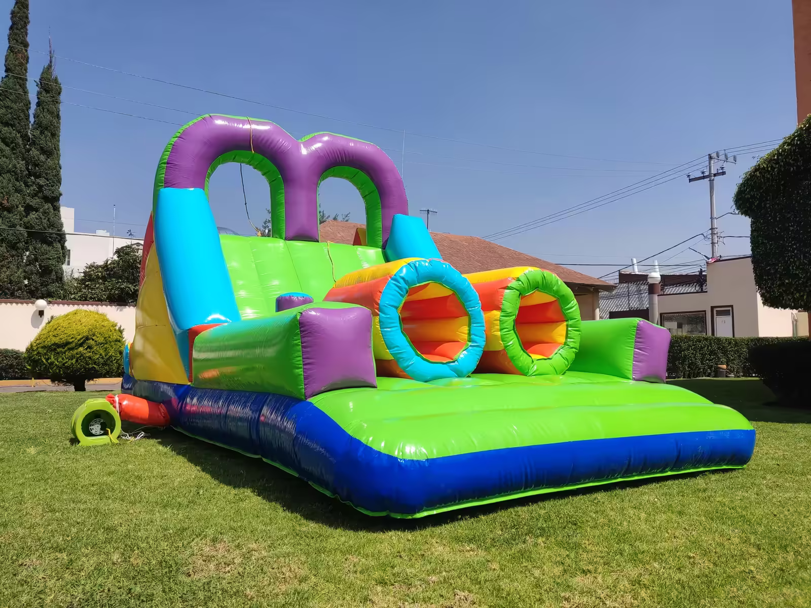 Inflable de circuito de obstáculos con túneles y tobogán instalado en un jardín para un evento