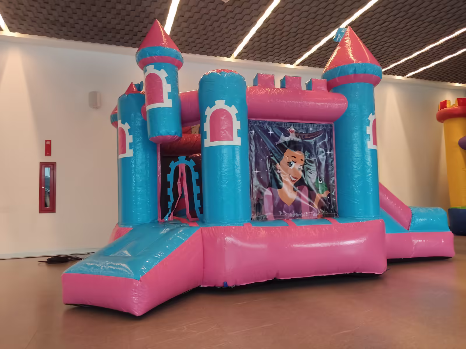 Inflable Castillo de Princesas en tonos rosa y turquesa instalado dentro de un salón de fiestas