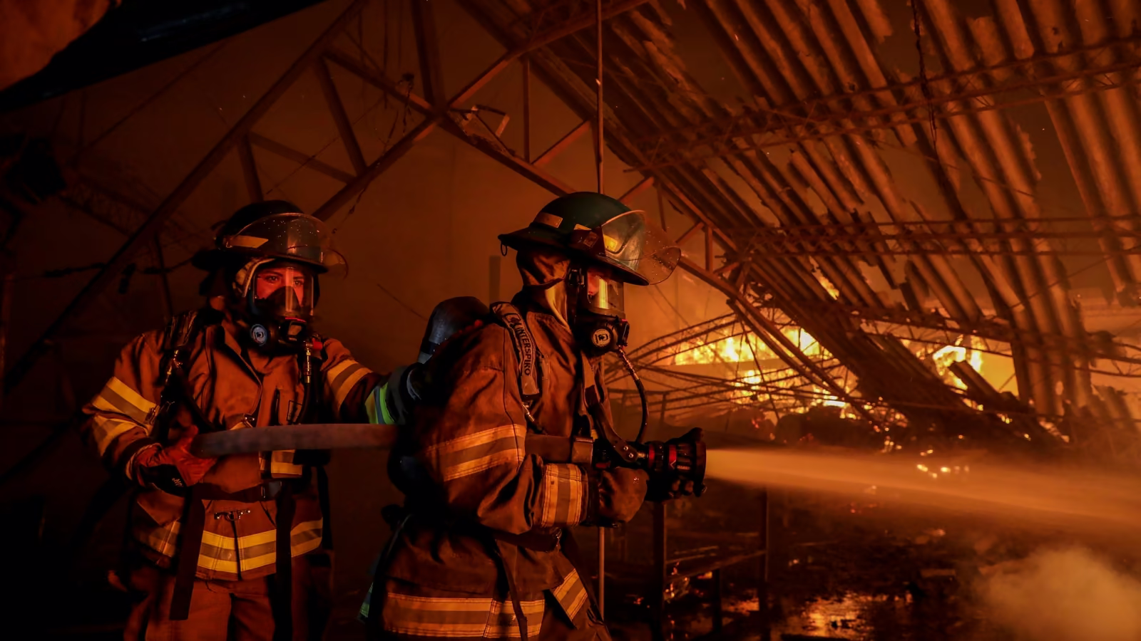 Dos bomberos con equipo de respiración autónoma atacan un incendio con una línea de manguera