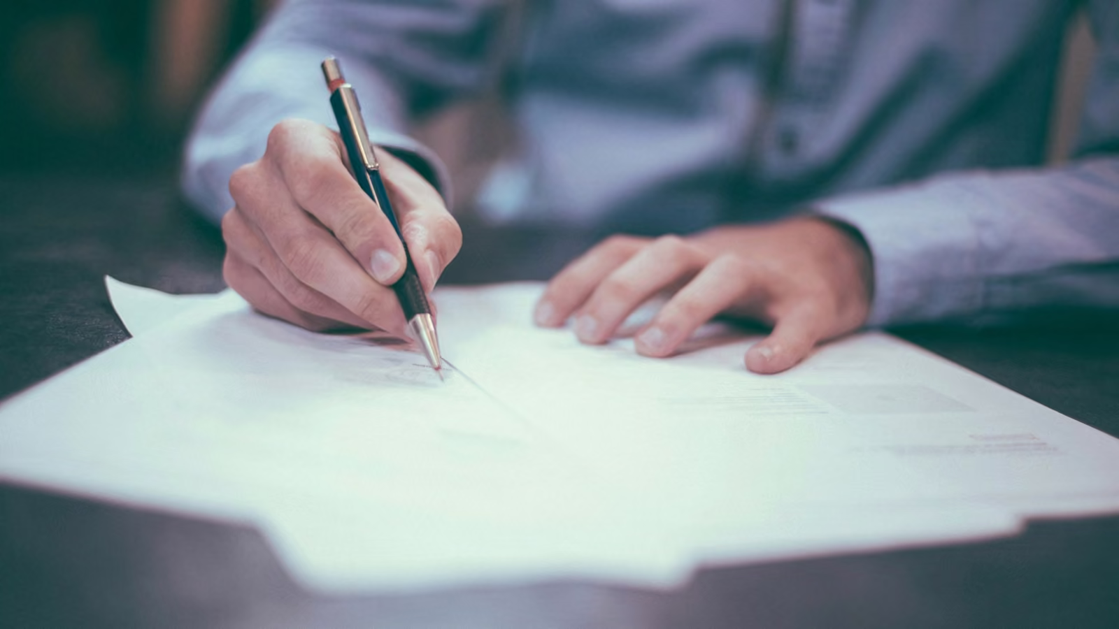 Mano firmando un documento sobre un escritorio